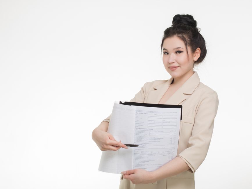 Smiling businesswoman in beige blazer holding and pointing to documents against white background.